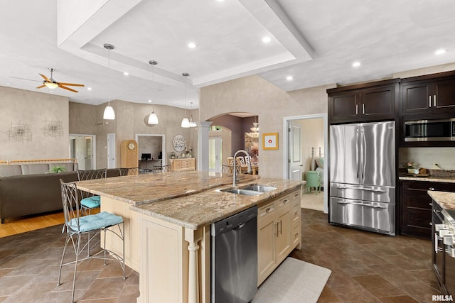 kitchen with sink, a center island with sink, a tray ceiling, a kitchen breakfast bar, and stainless steel appliances