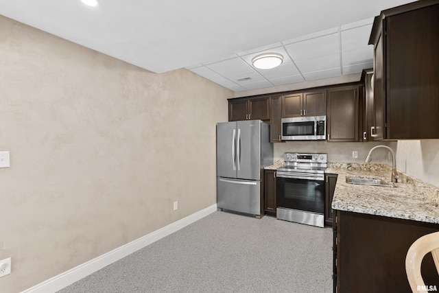 kitchen with sink, light stone counters, dark brown cabinets, appliances with stainless steel finishes, and a drop ceiling