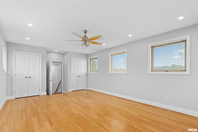 unfurnished bedroom with ceiling fan, light hardwood / wood-style flooring, and two closets