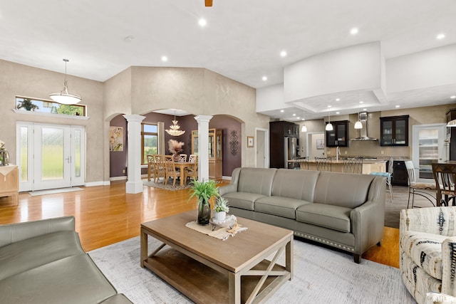 living room featuring decorative columns, a towering ceiling, sink, and light hardwood / wood-style flooring