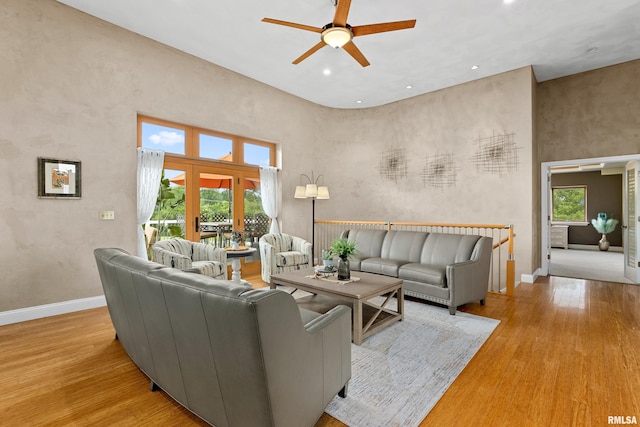 living room featuring ceiling fan, a towering ceiling, and light wood-type flooring