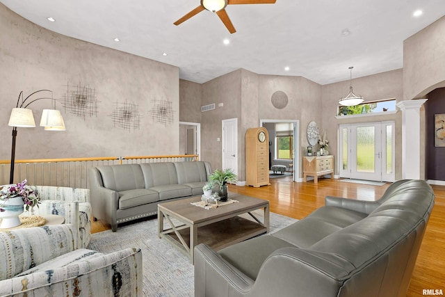 living room with ceiling fan, a towering ceiling, light hardwood / wood-style flooring, and ornate columns