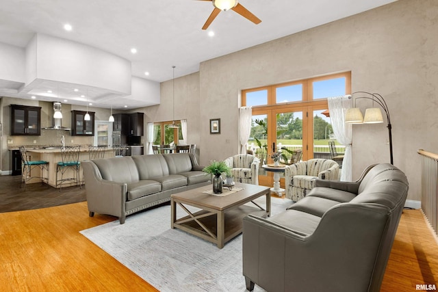 living room with ceiling fan, a towering ceiling, sink, and light hardwood / wood-style floors