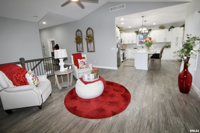 living room with lofted ceiling, wood-type flooring, and ceiling fan with notable chandelier