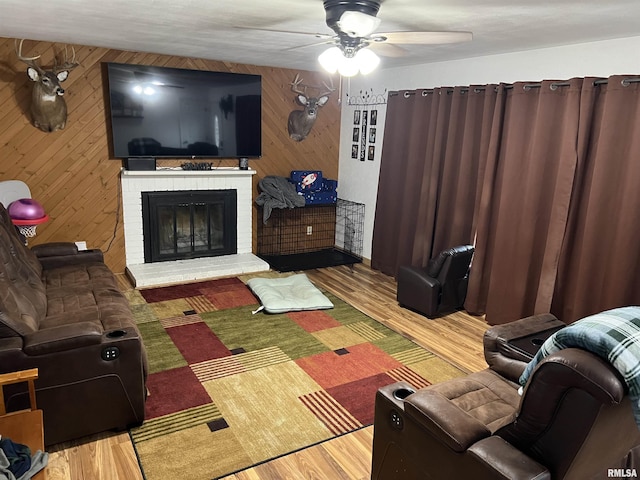 living room featuring ceiling fan, a fireplace, wood-type flooring, and wood walls