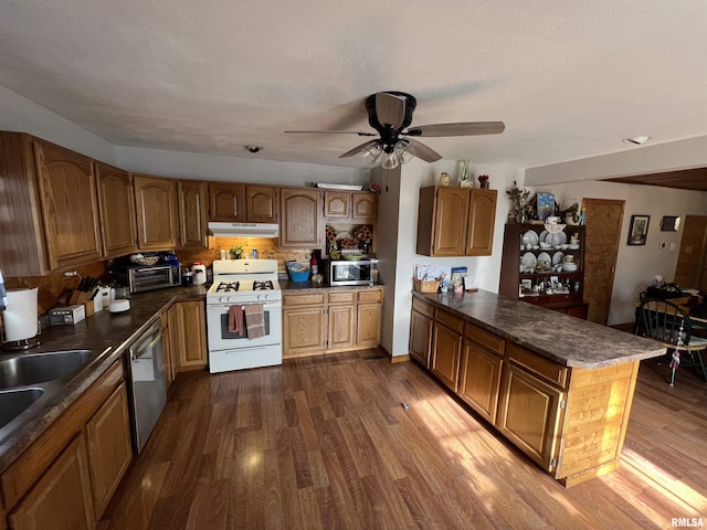 kitchen with appliances with stainless steel finishes, dark hardwood / wood-style flooring, kitchen peninsula, ceiling fan, and backsplash