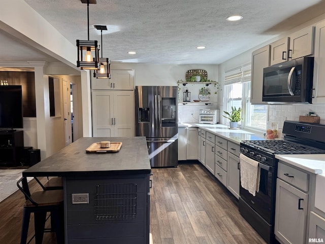 kitchen featuring black gas range oven, stainless steel fridge, hanging light fixtures, a center island, and dark wood-type flooring