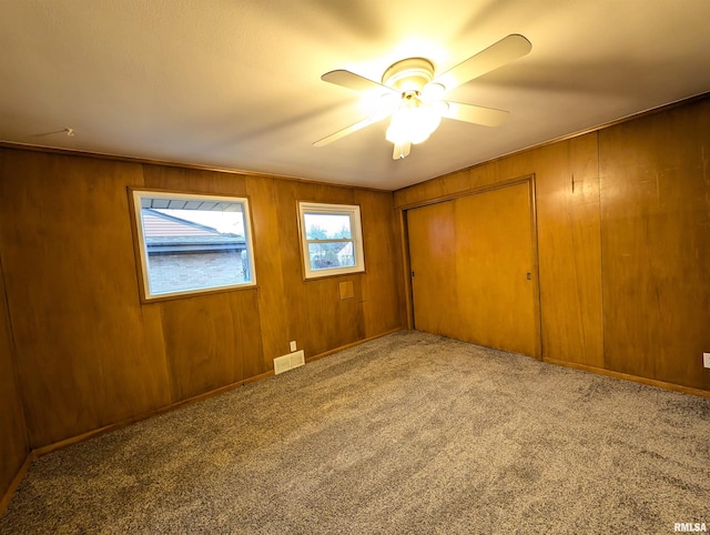 unfurnished bedroom with ceiling fan, carpet floors, a closet, and wood walls