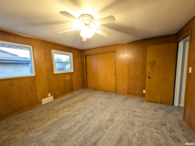 unfurnished bedroom with light colored carpet, a closet, ceiling fan, and wood walls