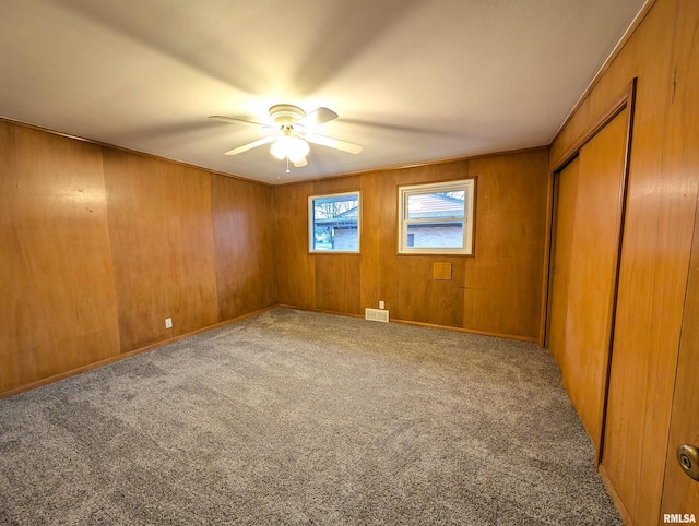 carpeted empty room featuring wooden walls and ceiling fan