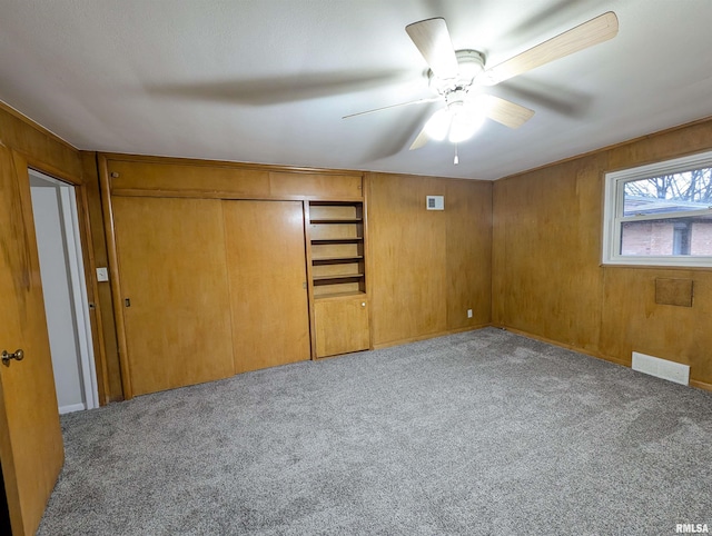 unfurnished bedroom featuring wooden walls, light colored carpet, and ceiling fan