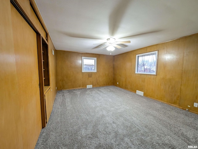 unfurnished room with ceiling fan, carpet flooring, and wood walls