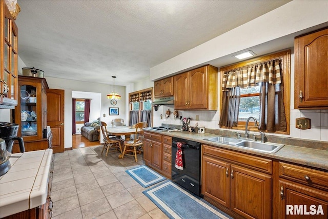 kitchen featuring light tile patterned flooring, decorative light fixtures, dishwasher, sink, and a textured ceiling