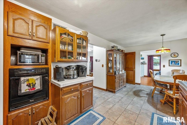 kitchen with light tile patterned flooring, decorative light fixtures, a textured ceiling, tile counters, and black oven