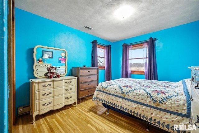 bedroom with a textured ceiling, light hardwood / wood-style flooring, and a baseboard radiator