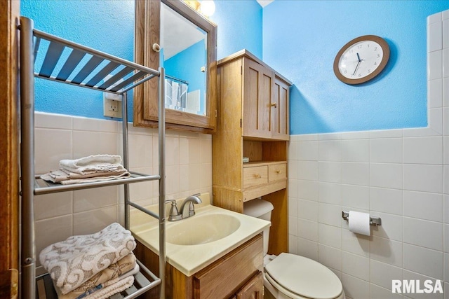 bathroom featuring vanity, tile walls, and toilet