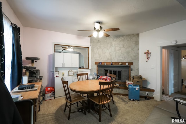 carpeted dining area with a stone fireplace and ceiling fan