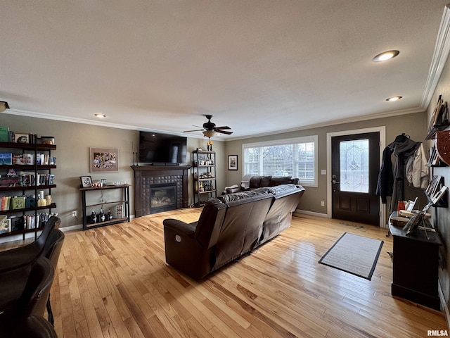 living room with crown molding, ceiling fan, a fireplace, and light hardwood / wood-style floors