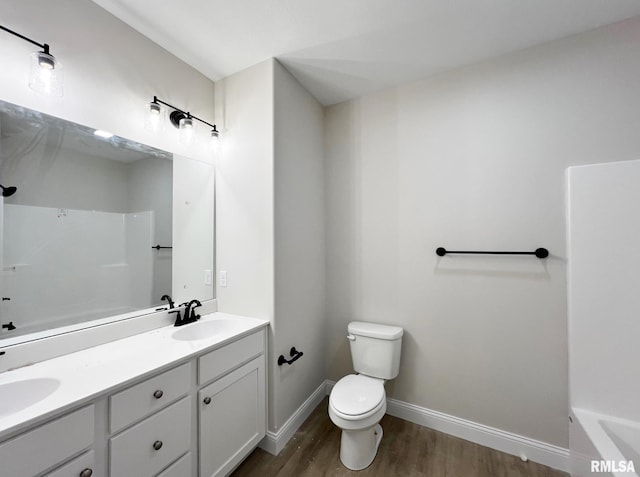 bathroom featuring toilet, baseboards, a sink, double vanity, and wood finished floors
