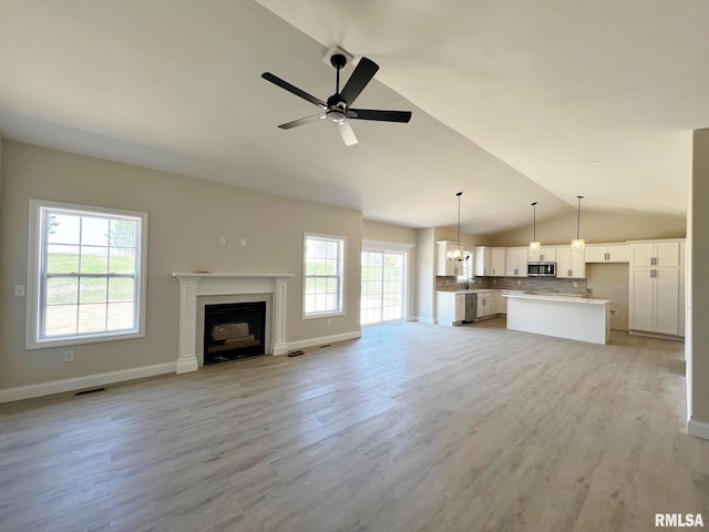 unfurnished living room with vaulted ceiling, a fireplace with flush hearth, light wood-style flooring, visible vents, and ceiling fan