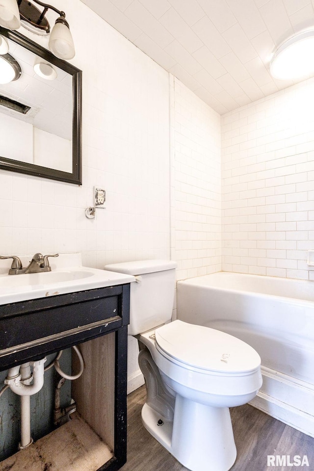 bathroom with wood-type flooring, toilet, vanity, and a tub