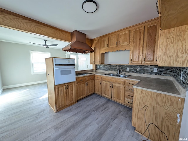 kitchen featuring sink, tasteful backsplash, light hardwood / wood-style flooring, island exhaust hood, and oven