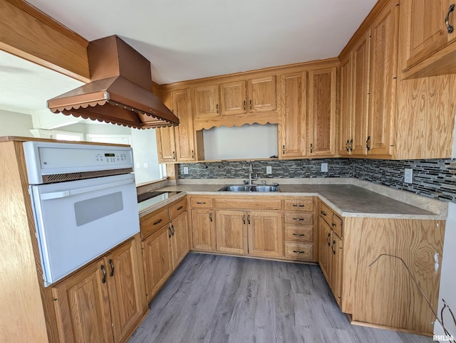 kitchen with sink, white oven, tasteful backsplash, light hardwood / wood-style floors, and island exhaust hood