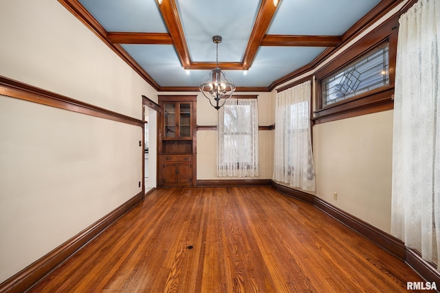 empty room featuring dark wood-type flooring, coffered ceiling, crown molding, a chandelier, and beam ceiling