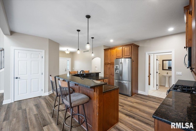 kitchen featuring appliances with stainless steel finishes, dark hardwood / wood-style floors, pendant lighting, dark stone counters, and a kitchen island with sink