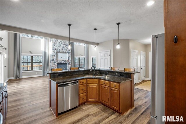 kitchen with appliances with stainless steel finishes, sink, dark stone countertops, hanging light fixtures, and light hardwood / wood-style flooring