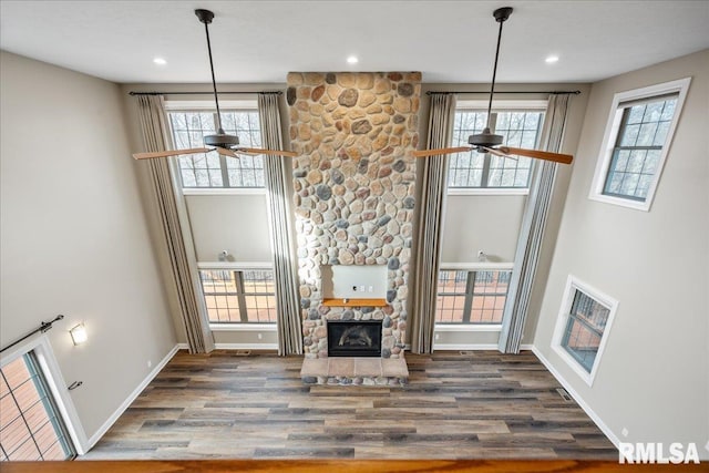 unfurnished living room with dark hardwood / wood-style flooring, a stone fireplace, and ceiling fan