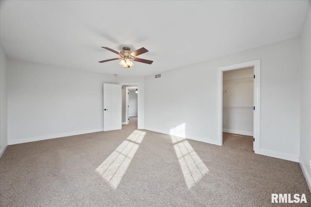 unfurnished bedroom featuring a walk in closet, carpet floors, ceiling fan, and a closet