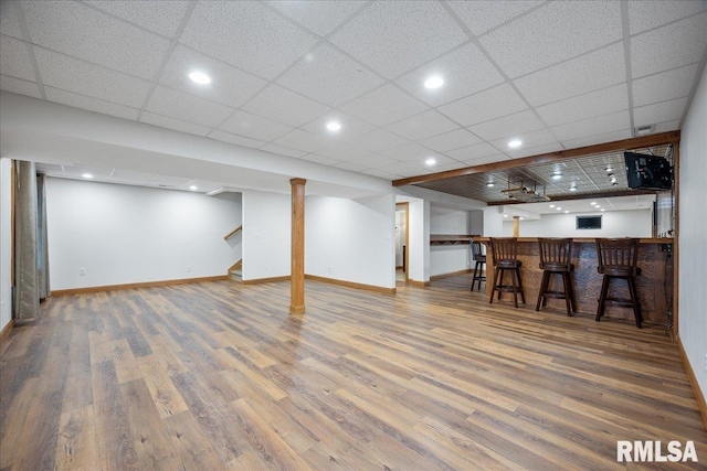 basement with bar, hardwood / wood-style flooring, and a paneled ceiling