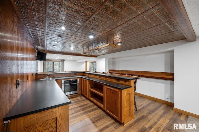 kitchen with hardwood / wood-style flooring, a breakfast bar area, oven, and kitchen peninsula