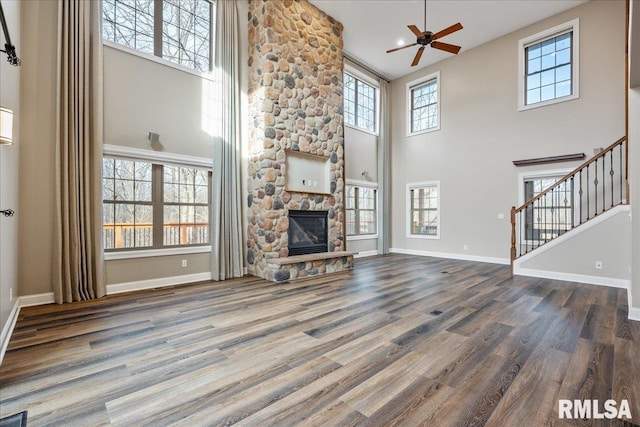 unfurnished living room featuring a high ceiling, a stone fireplace, hardwood / wood-style floors, and ceiling fan