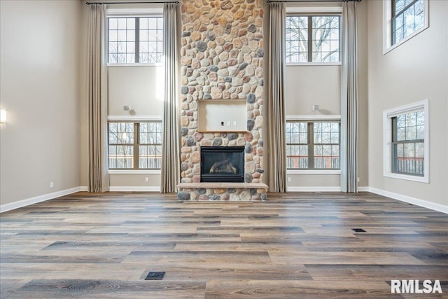 unfurnished living room featuring a high ceiling, a stone fireplace, and hardwood / wood-style floors