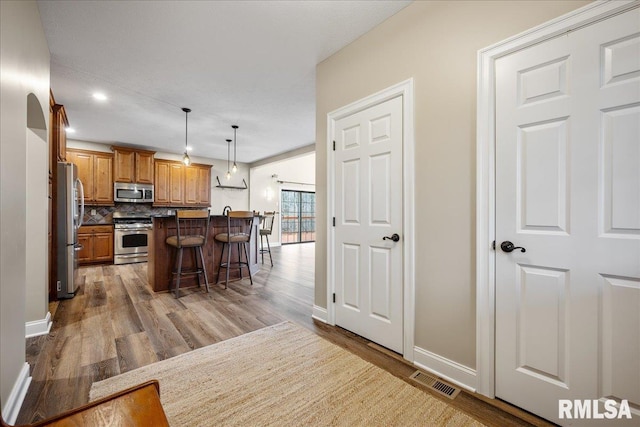 kitchen featuring light hardwood / wood-style flooring, hanging light fixtures, stainless steel appliances, a center island, and a kitchen bar