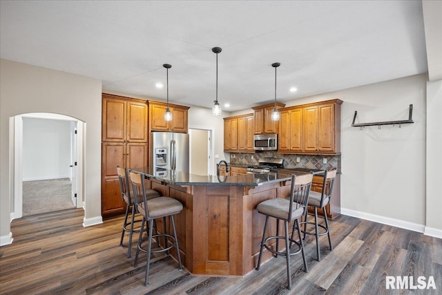 kitchen with appliances with stainless steel finishes, a breakfast bar, pendant lighting, tasteful backsplash, and a kitchen island with sink