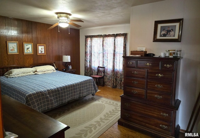 bedroom with ceiling fan, hardwood / wood-style floors, and wooden walls