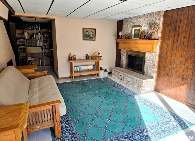 living room featuring a drop ceiling, a fireplace, and wood walls