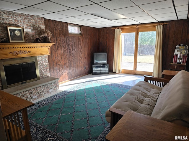 living room with a brick fireplace, a paneled ceiling, and wood walls