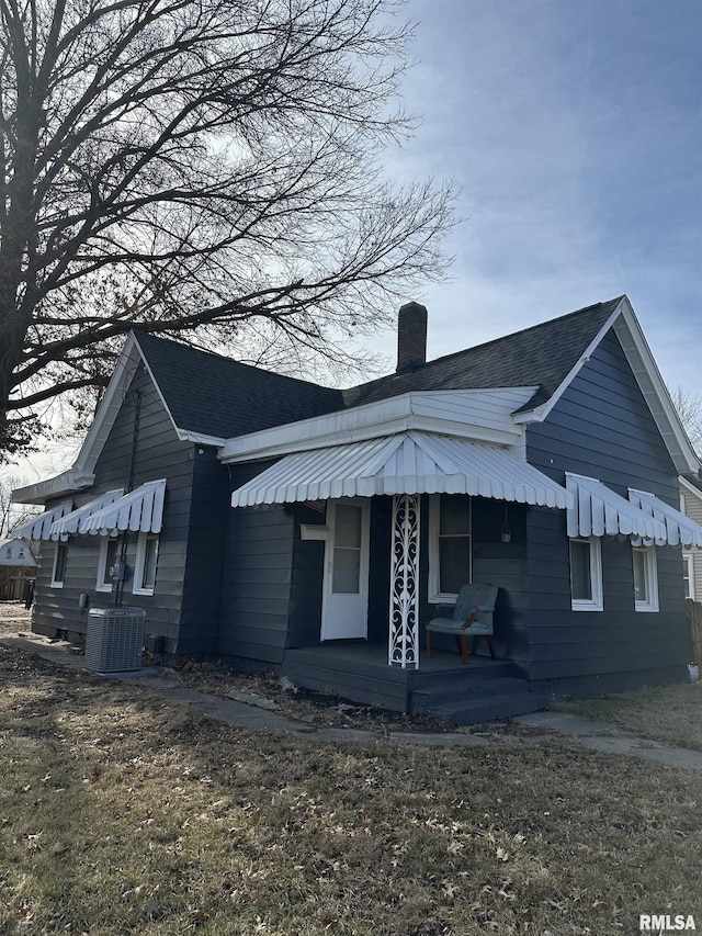 view of front of property featuring central air condition unit, covered porch, a shingled roof, and a chimney