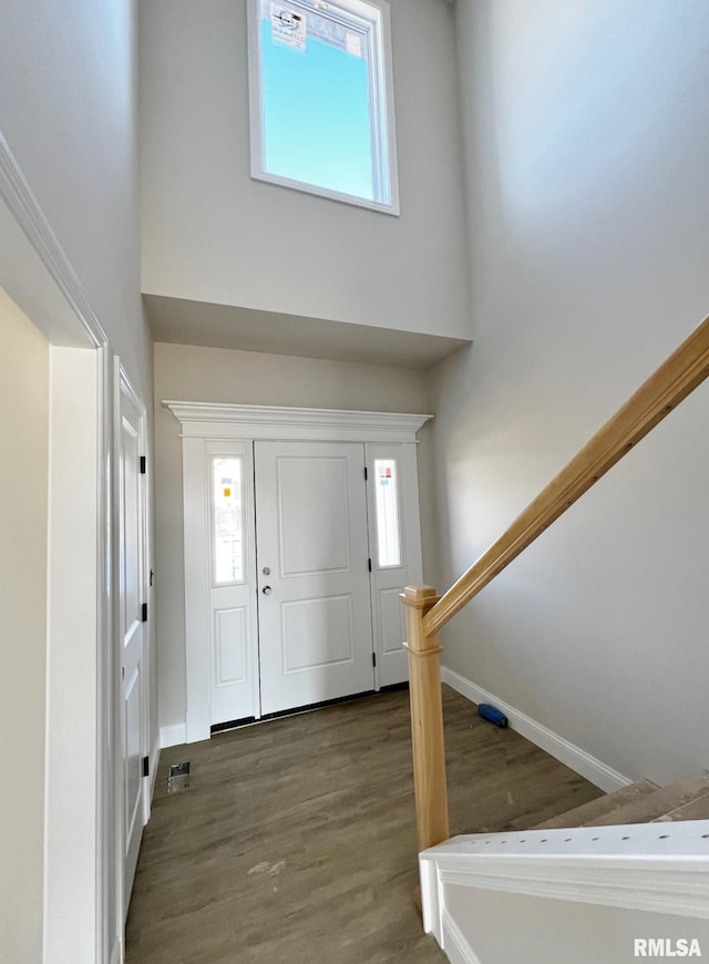 foyer entrance with stairway, baseboards, wood finished floors, and a towering ceiling