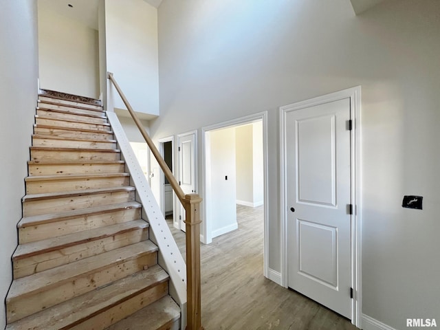 stairway with a high ceiling, wood finished floors, and baseboards