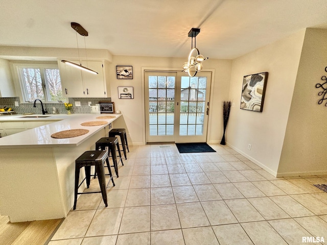 kitchen with a breakfast bar, pendant lighting, white cabinets, backsplash, and kitchen peninsula