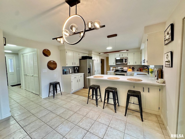 kitchen with appliances with stainless steel finishes, a breakfast bar, sink, white cabinets, and kitchen peninsula