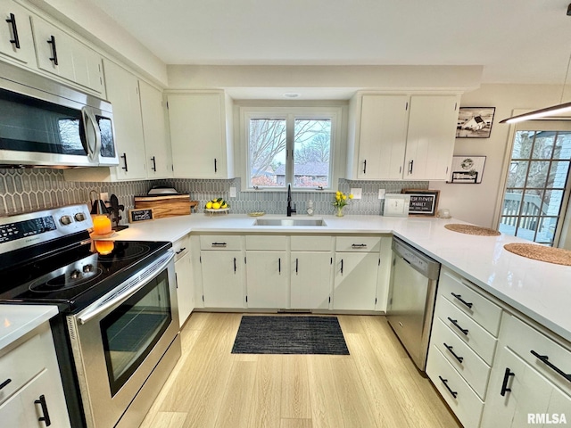 kitchen featuring sink, tasteful backsplash, white cabinetry, light wood-type flooring, and appliances with stainless steel finishes