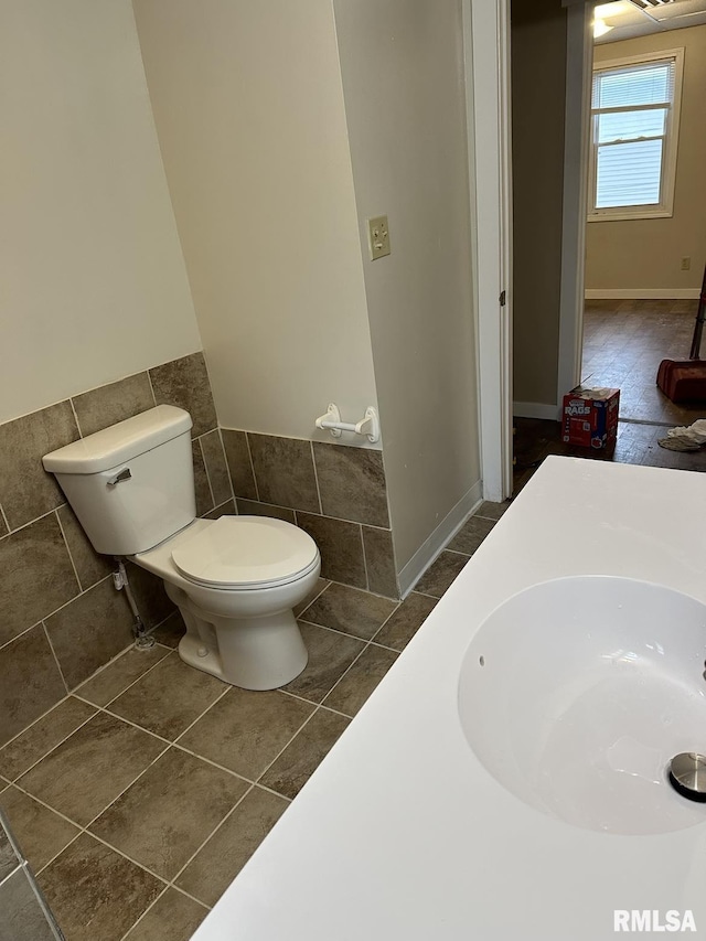 bathroom with toilet, tile patterned flooring, sink, and tile walls