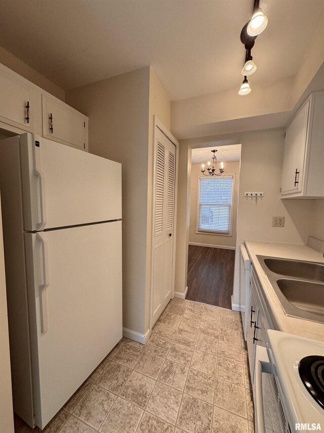 kitchen with sink, white cabinets, hanging light fixtures, white appliances, and an inviting chandelier