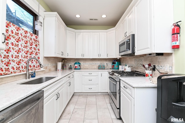 kitchen with white cabinetry, stainless steel appliances, sink, and light stone counters